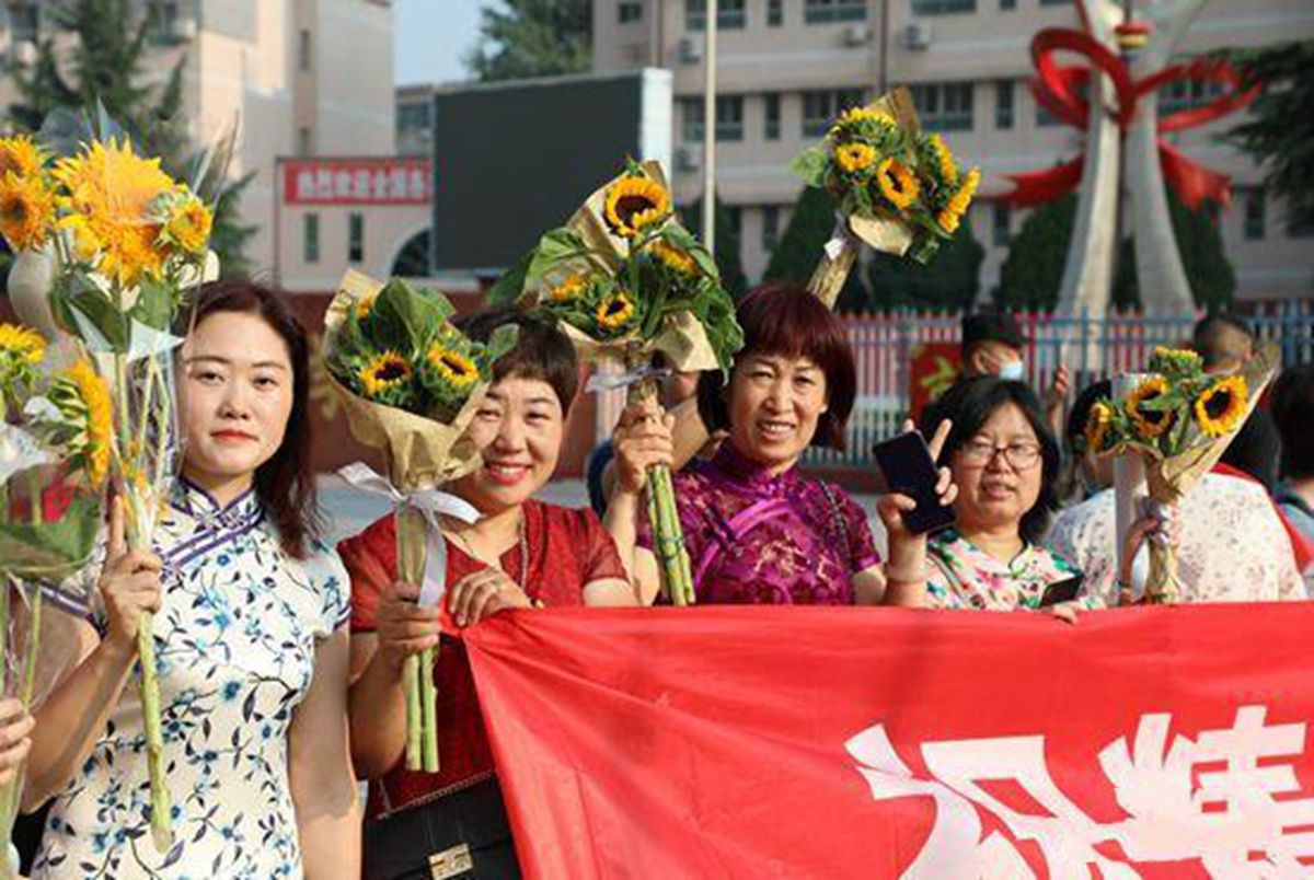 看看高考父母的穿搭：爸爸穿马褂，妈妈穿旗袍，手里还举着向日葵